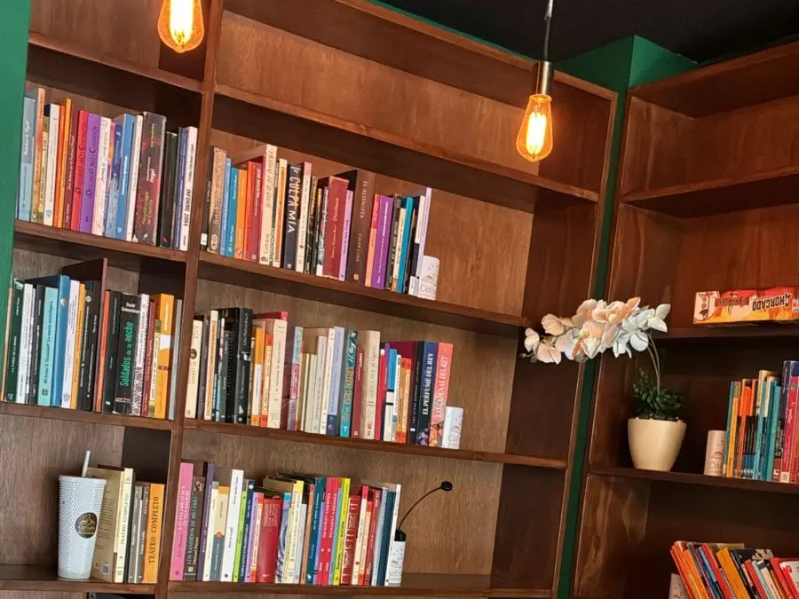 Los libreros del café llenos de novelas y libros de todos los colores, con un foco cálido encendido