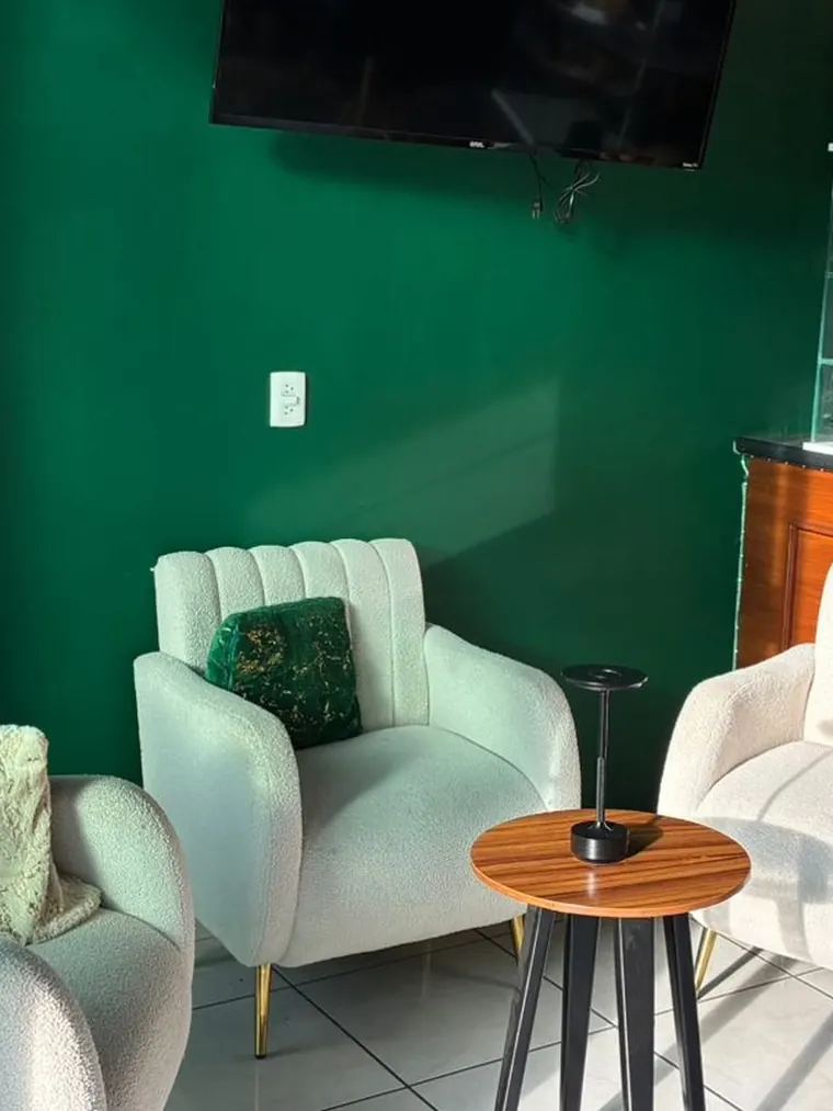 Dos sillones color crema con cojines verdes y una mesita de madera, contra la pared verde del café